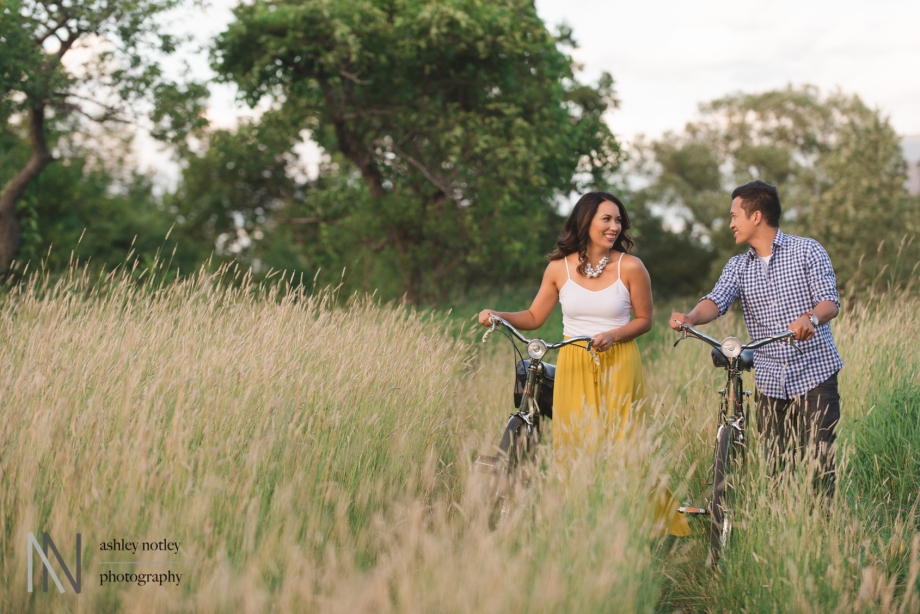 Couple walking bikes in long grass at the experimental farm during their engagement photo session