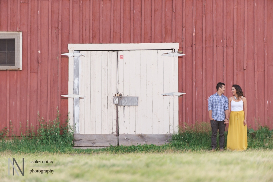 Couple holding hands in front of red barn at the experimental farm
