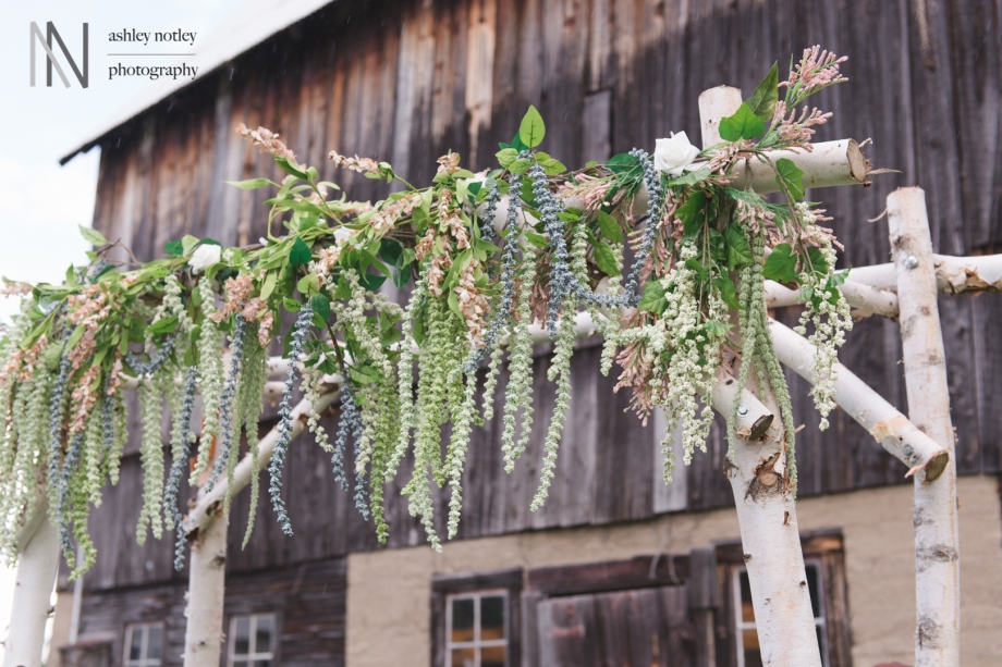 Florals around a birch alter at ceremony by a rustic barn