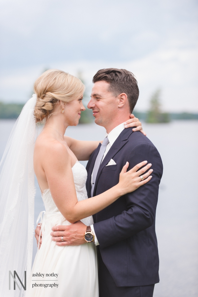 Bride and groom embracing by waterfront at country farm house wedding